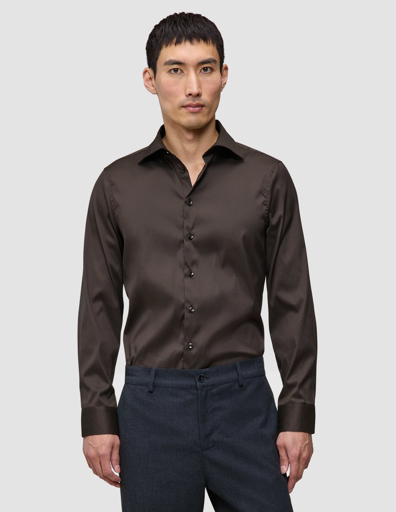 En mann har på seg en mørkebrun Elevated Shirt Slim, som er stappet inn i mørke bukser.